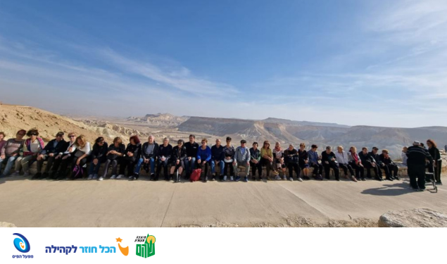 קבוצת אנשים יושבת על חומה וברקע נוף מדברי